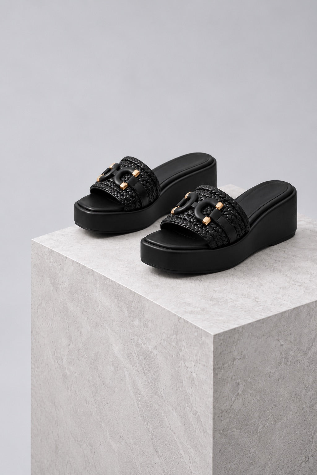 Black woven platform wedge slides on a grey stone plinth