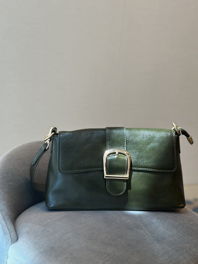 Paired Valora Buckle Sling Bag in deep green, with a buckled front flap, resting on a grey chair