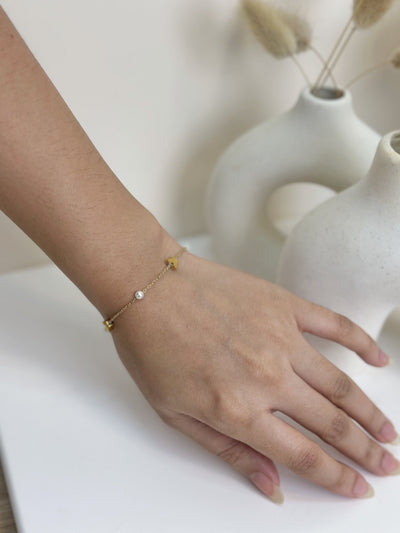 Paired Vianne Bracelet in gold-tone, worn on the wrist with butterfly charms and small white beads on a fine chain