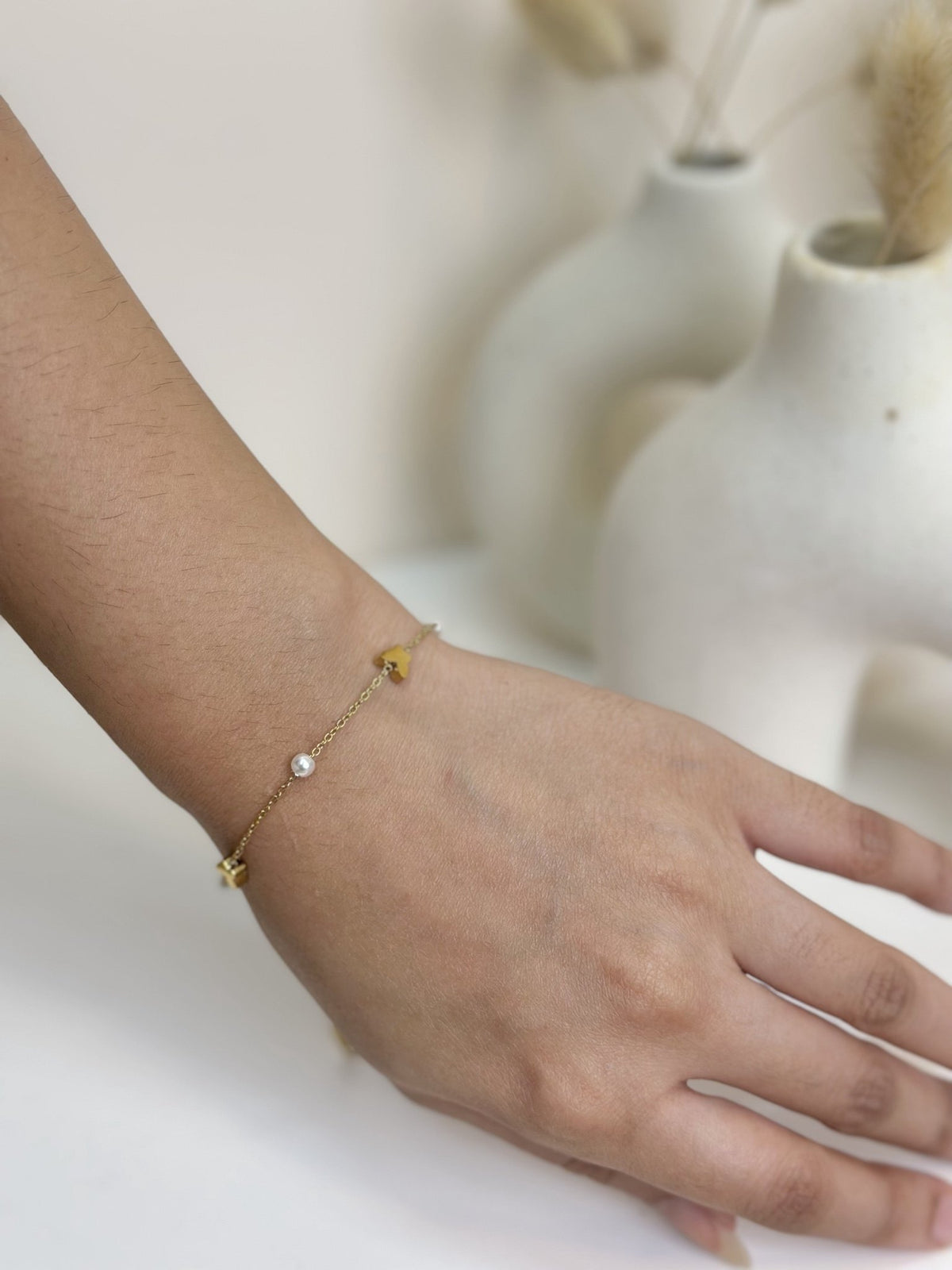 Paired Vianne Bracelet in gold-tone, worn on the wrist, a fine chain with butterfly charms and a white bead