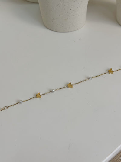 Paired Vianne Bracelet in gold-tone, laid flat to show the fine chain with butterfly charms and white beads alternating