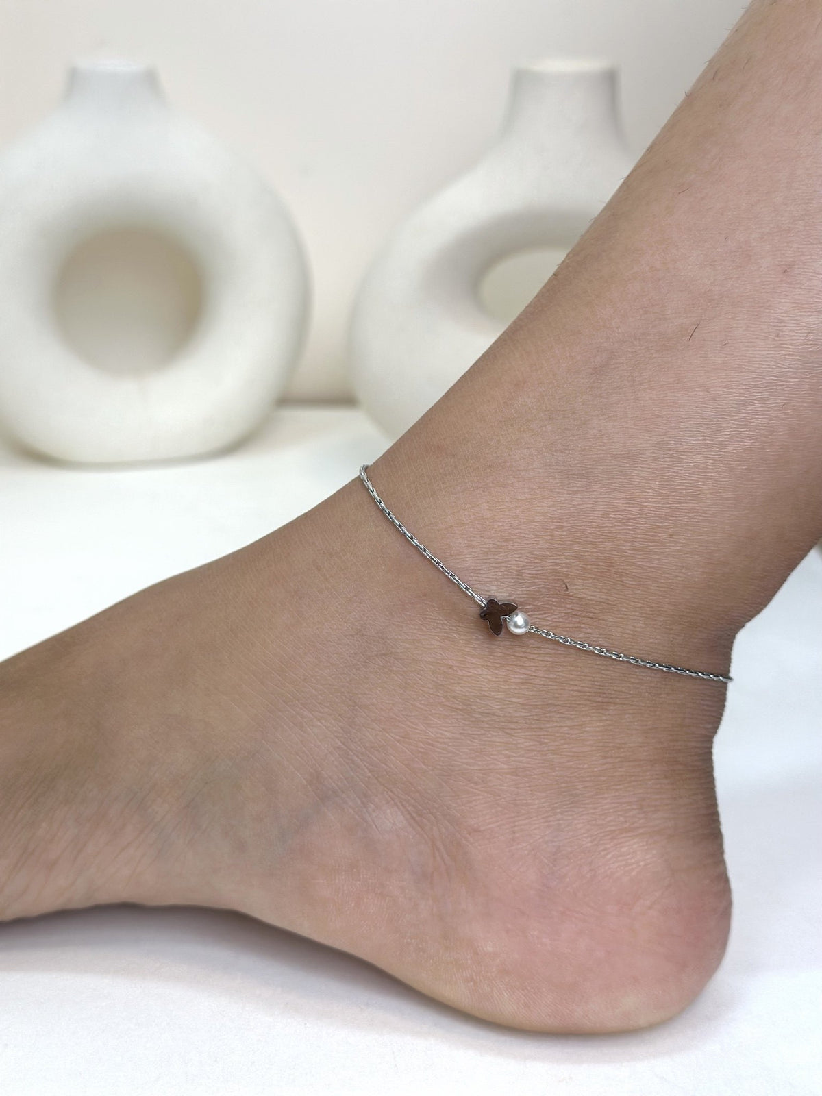 Paired Violette Anklet in silver-tone, worn on the ankle with a small dark charm and round white bead