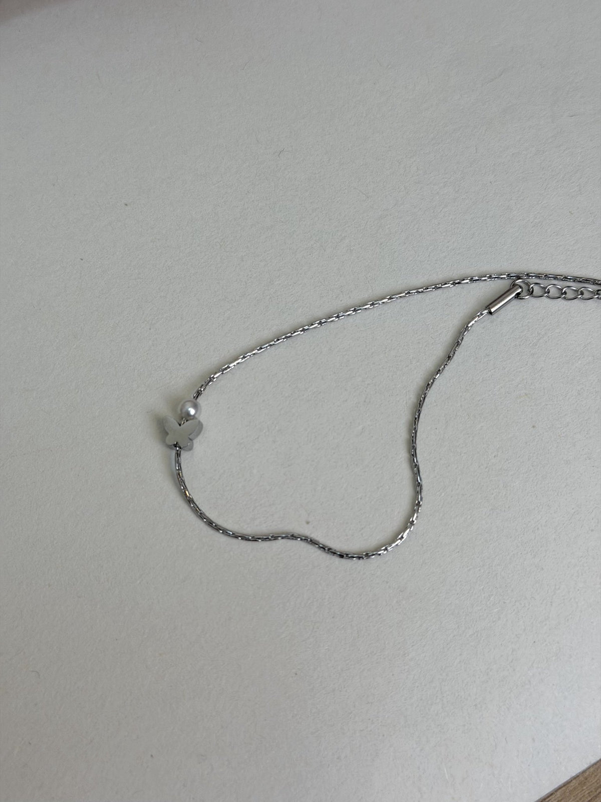 Paired Violette Anklet in silver-tone, laid flat showing the fine chain, charm and adjustable end
