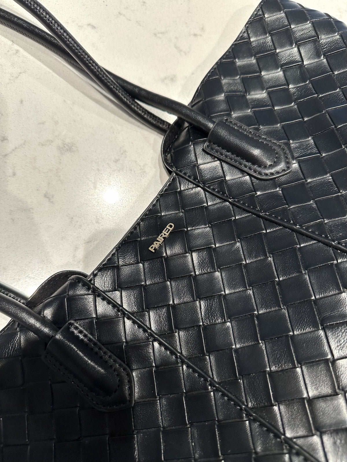 Paired Virelle Woven Bag in black, close-up of the woven texture, rolled handle and small logo plate