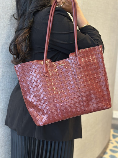Paired Virelle Woven Bag in maroon, worn on the shoulder with a rolled handle over a black jacket